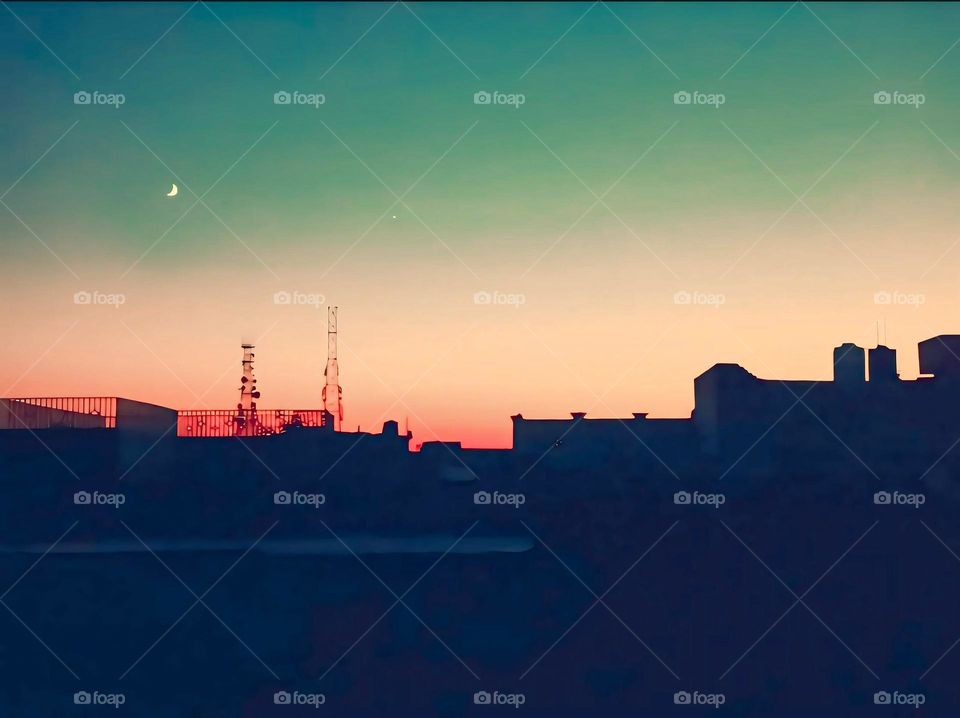 a view of Roof tops at Sunset with Crescent Moon and Evening Sky