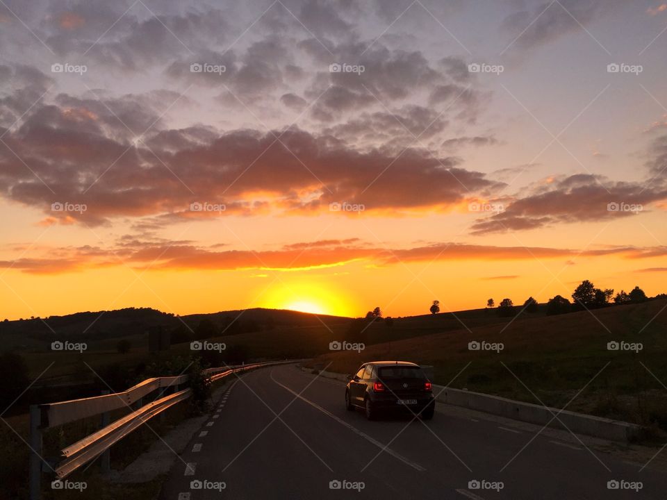 Car driving on an empty road in the mountains during golden hour in summer