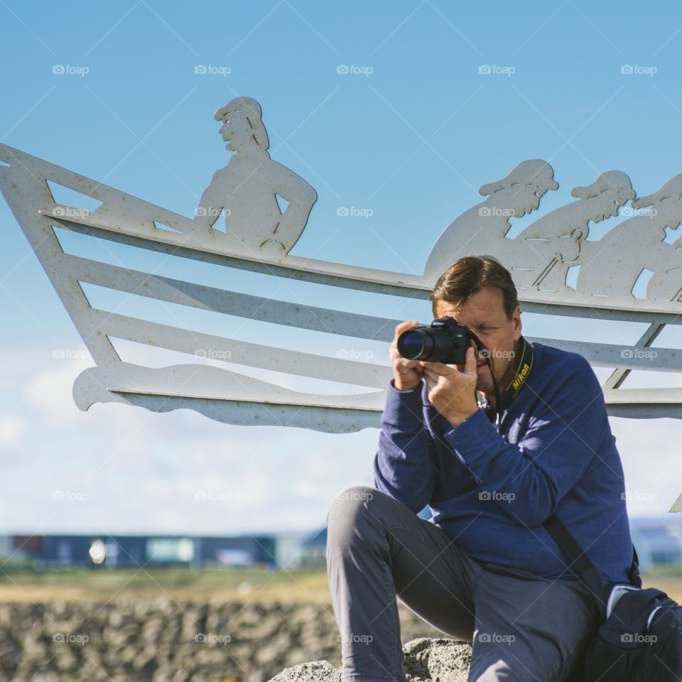 Man photographer taking pictures with sailboat in the background 