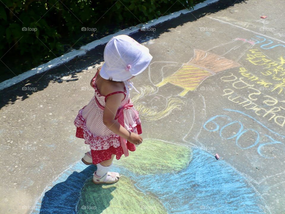little girl draws with colorful chalk bright drawings on the pavement