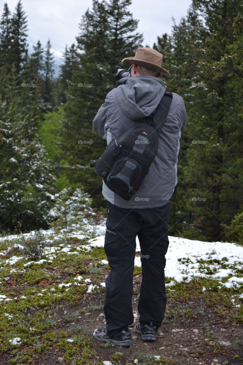 Male photographer photographing nature in the Canadian Rocky Mountains alpine meadow in spring with snow melt