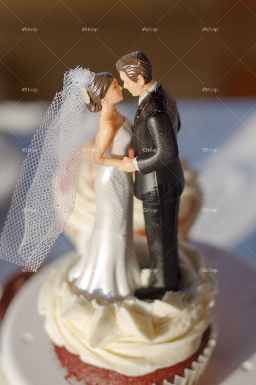 A bride and groom figurine sits on top of a wedding cupcake at a wedding reception waiting to be eaten