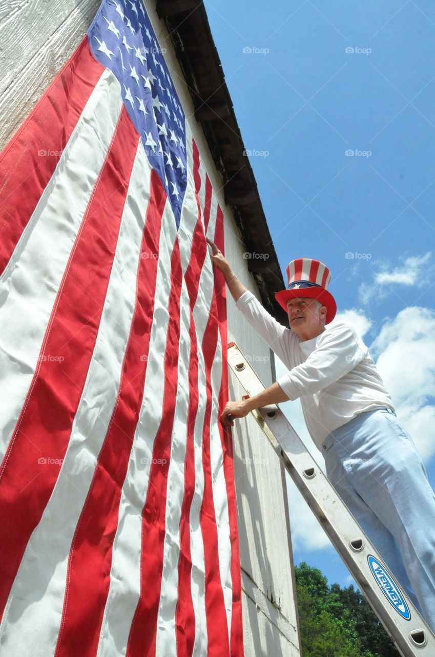 Senior man hangs huge American flag wearing an Uncle Sam's hat