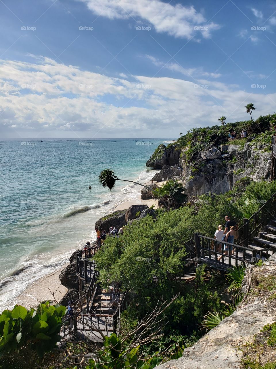 View from above, stunning beach with lush green cliffs, palm trees, blue ocean, and cloudy skies in Mexico.
