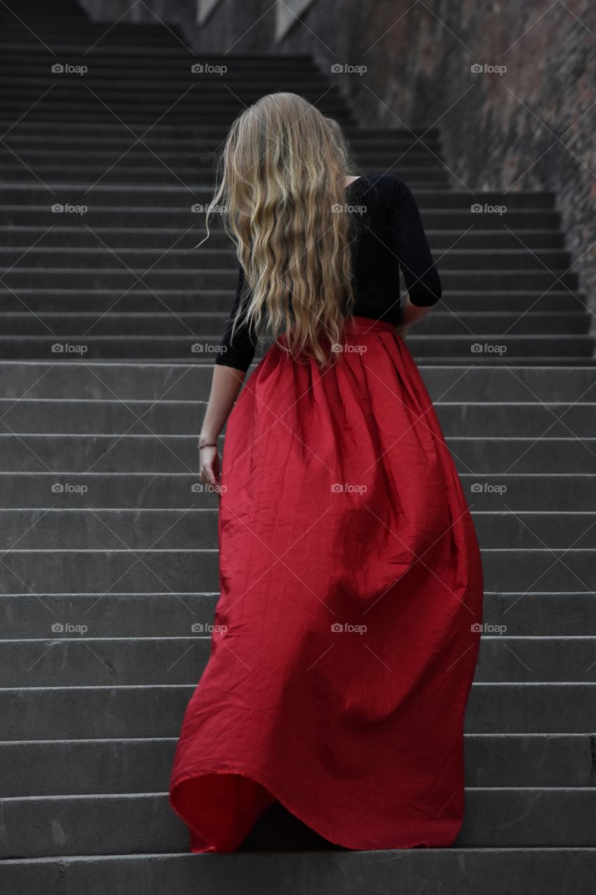 Blonde long hair woman in long red skirt standing on the stairs in old Prague