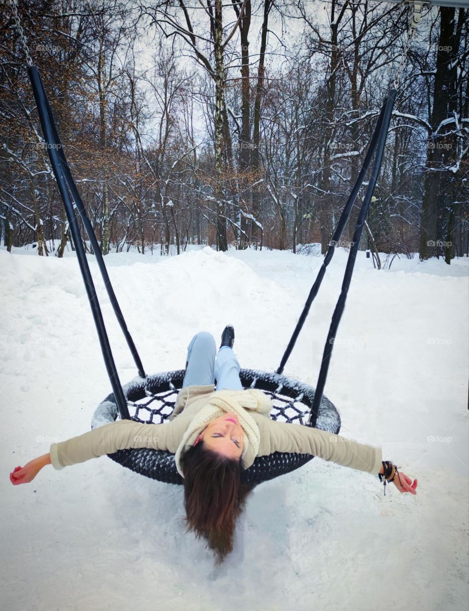 Winter. Winter park in the snow. A woman lies on a hanging swing with outstretched arms. Feeling of flight, freedom and peace. Cold beauty of nature in winter
