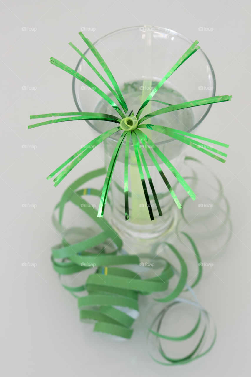 Glass with festive green straw and serpentine , white background 