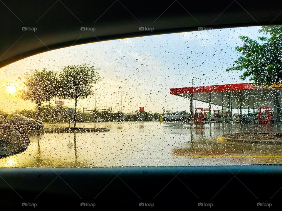 A magical sunset after a storm creating a canvas of reflections framed and textured by a passenger car wet window view.