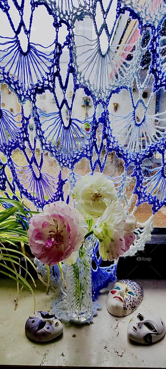 An artfully crocheted lacey curtain made with multicolor wool ranging from white to shades of indigo to violet to purple adorns a window of the house in „Bavaria“ that we have visited before in our photographic journey. 2023. Hypnotic Productions