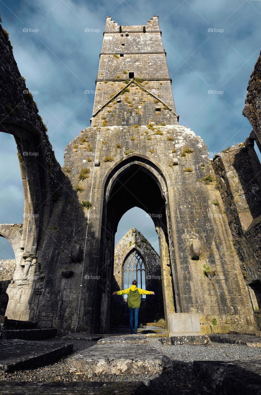 Girl in yellow jacket standing under arch of historical landmark Claregalway Friary in county Galway, Ireland