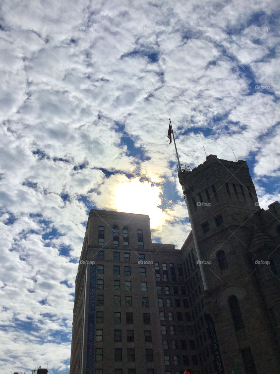 Sky clouds and sunshine over building with flag 