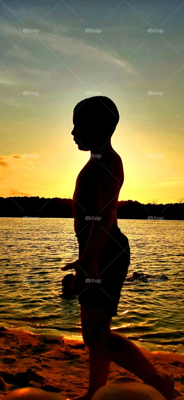 foap mission vertical capture young boy walking beach in silhouette during golden sunset another child in water in background