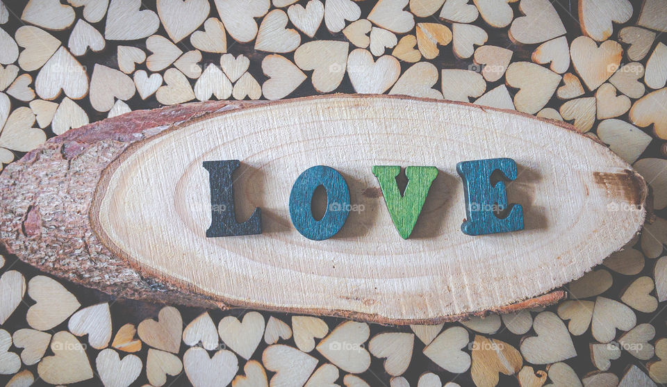 The word “love” spelled out in wooden letters, on a live edge, wood plaque, surrounded by wooden hearts 