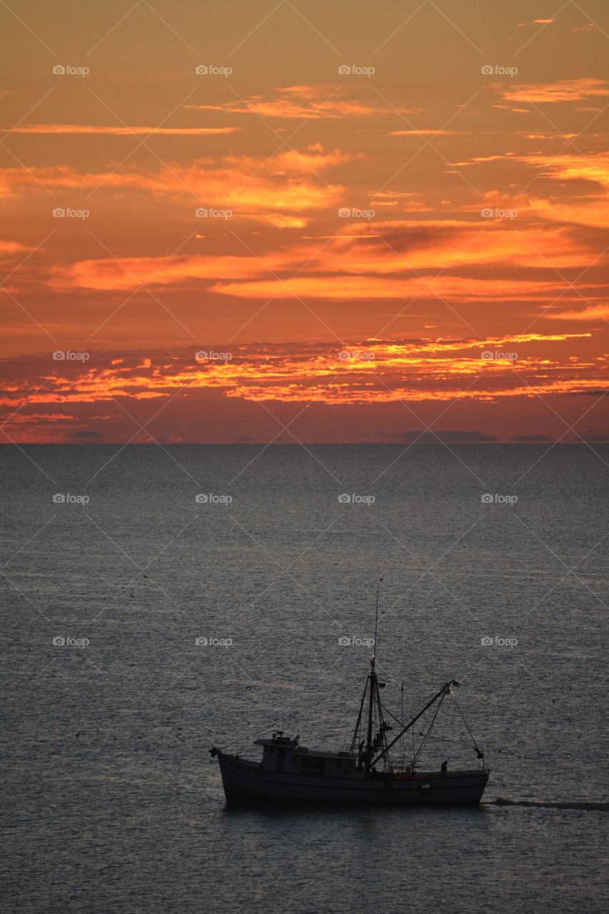 A shrimp boat trawling the Atlantic Ocean at sunrise. 