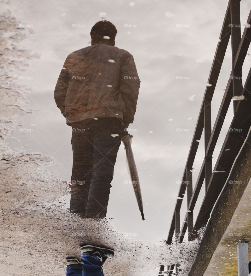 a man with an umbrella is reflected in a puddle