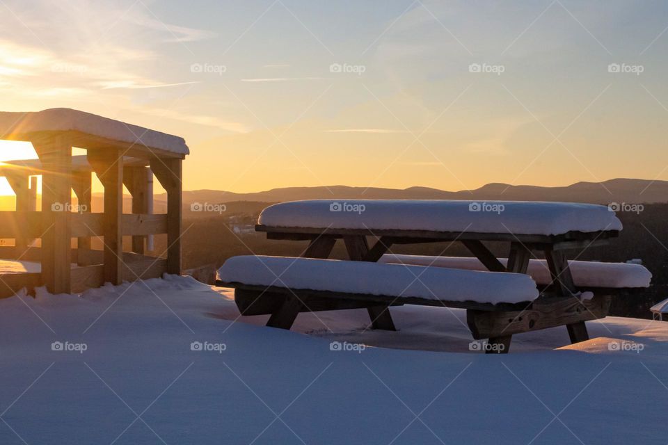 Golden hour in the mountains of New England 2022. A crisp evening with a snow covered picnic table and landscape.