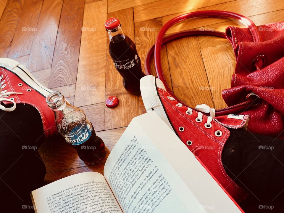 Coca Cola bottles on hardwood floor with red sneakers and a red leather bag and book.