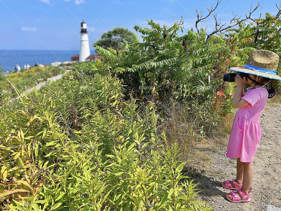 Little girl photographs light house, taking photographs on vacation with a toddler, making memories with photography