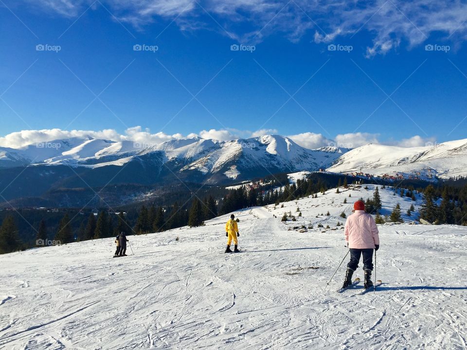 People skiing on a sunny day with blue sky and snowy mountains in the background 