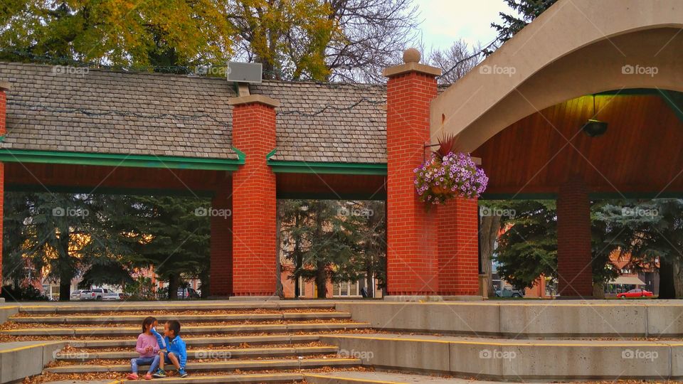 Sibling sitting on steps in park during autumn