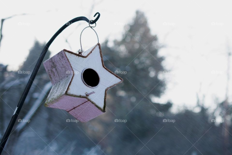 Star shaped bird house swings in wind on a snowy winter morning.