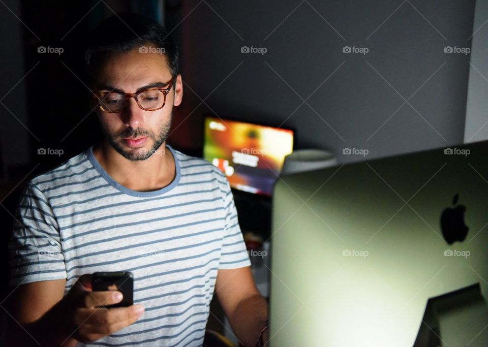 Young man sitting in front of laptop with mobile phone in hand