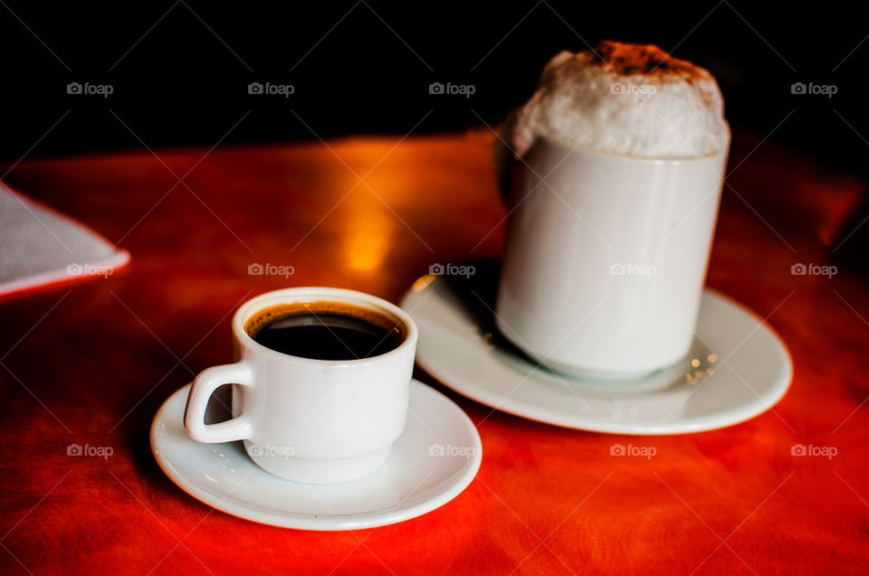 White espresso cup alongside white cappuccino mug on orange wooden table