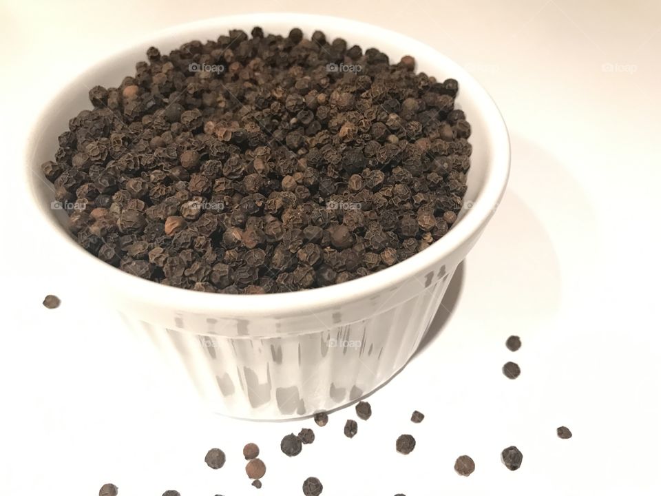 Black pepper in a bowl on white background 