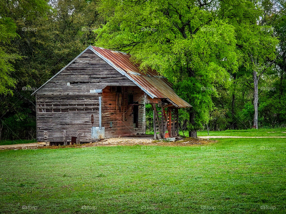 A weathered old wooden barn sits in a green field along a rural country road
