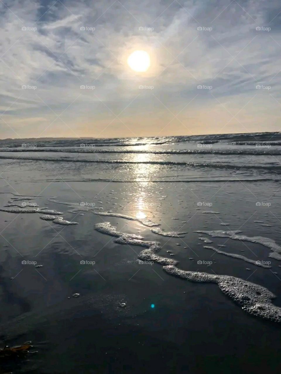 The sea splashes white foam on the sand of the beach on a sunny day.