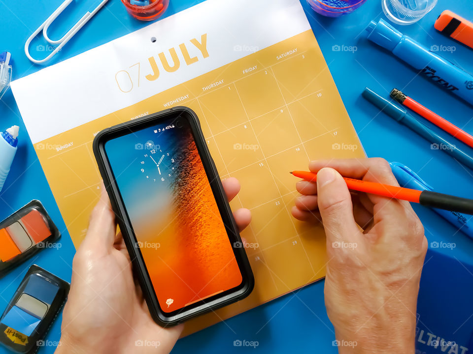 Planning- orange and blue theme.  Man holding cellphone and getting ready to write on a calendar.