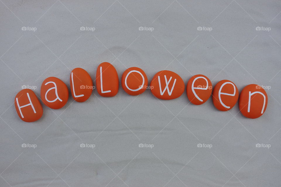 Halloween word with orange colored stones over white sand 