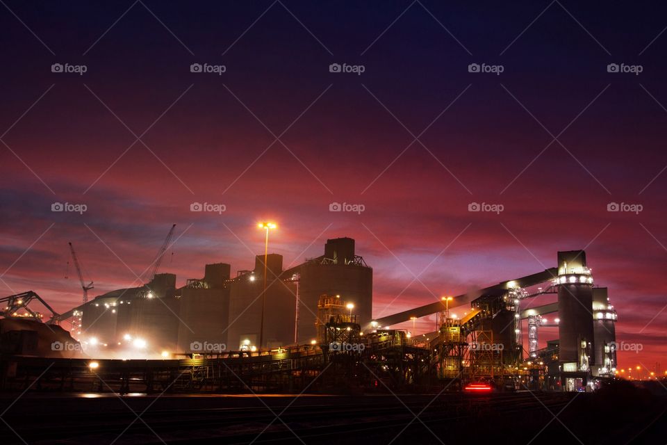 An industrial oil refinery with smoking chimneys and lit up at night.