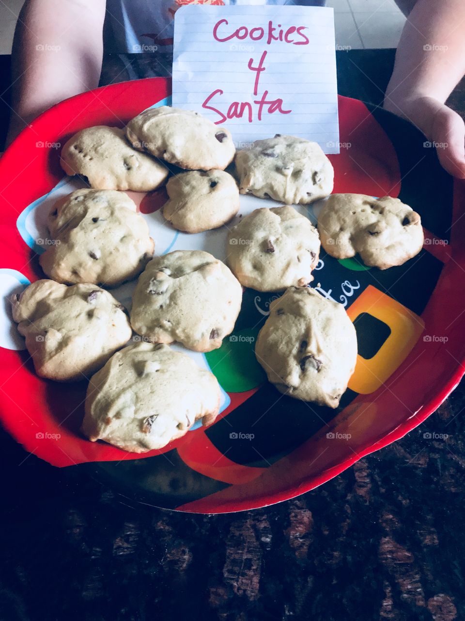 Cookies for Santa, A plate full of delicious chocolate chip cookies on a Christmas Santa Clause plate.  Child holding a plate of Cookies for Santa.