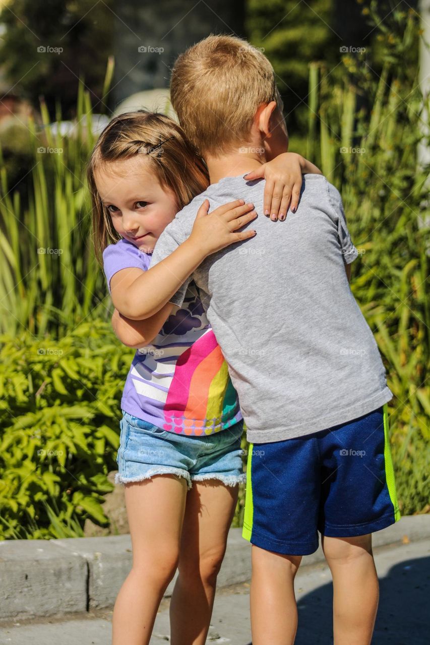 Young girl and boy toddler hugging in front of a grassy lake on a warm summer day in Oregon 