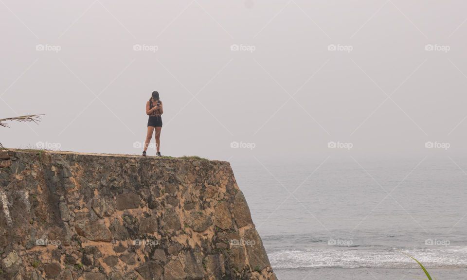 Be alone with the phone at morning beach side at galle fort on foggy day. Sri lanka
