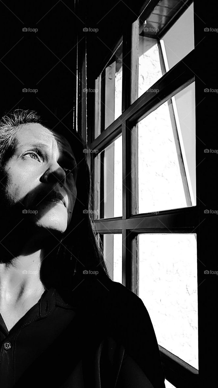 Selfie B&W with shadows of Woman with melancholy expression looking out the window at the street.