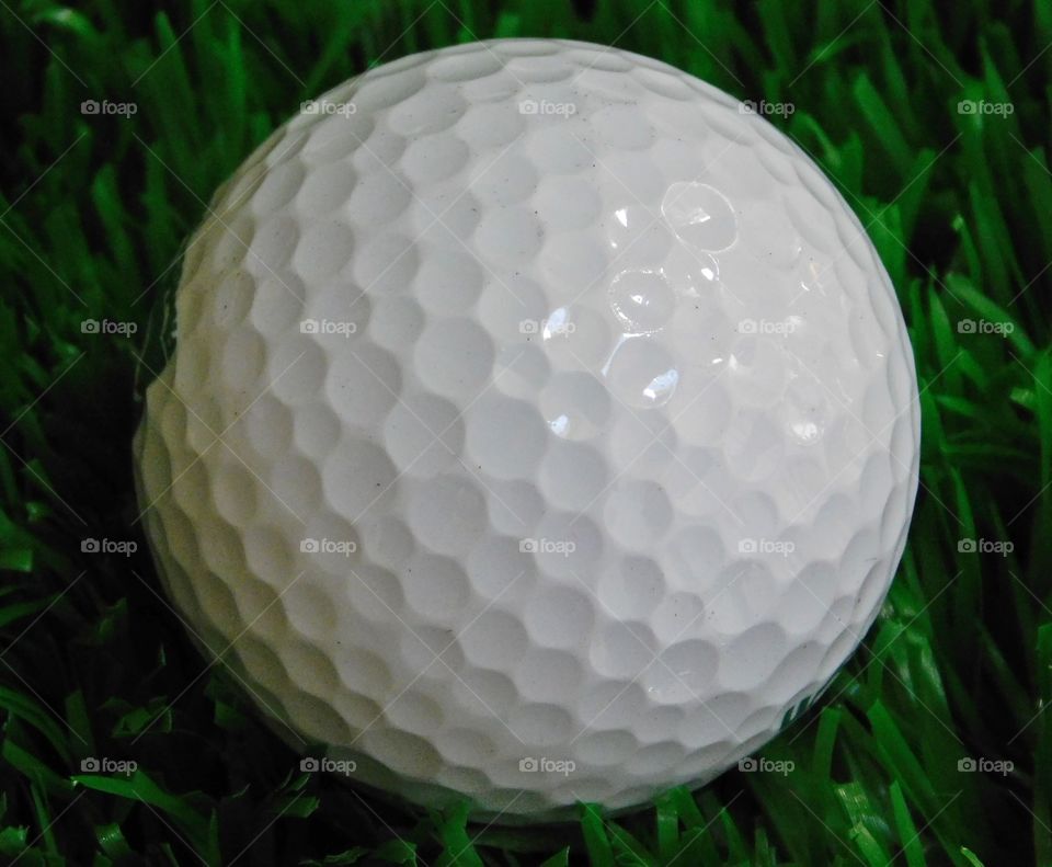 World in macro - A macro shot of a golf ball on the green during a golf tournament. The golf ball has hundreds of dimples which make it ergonomic. 