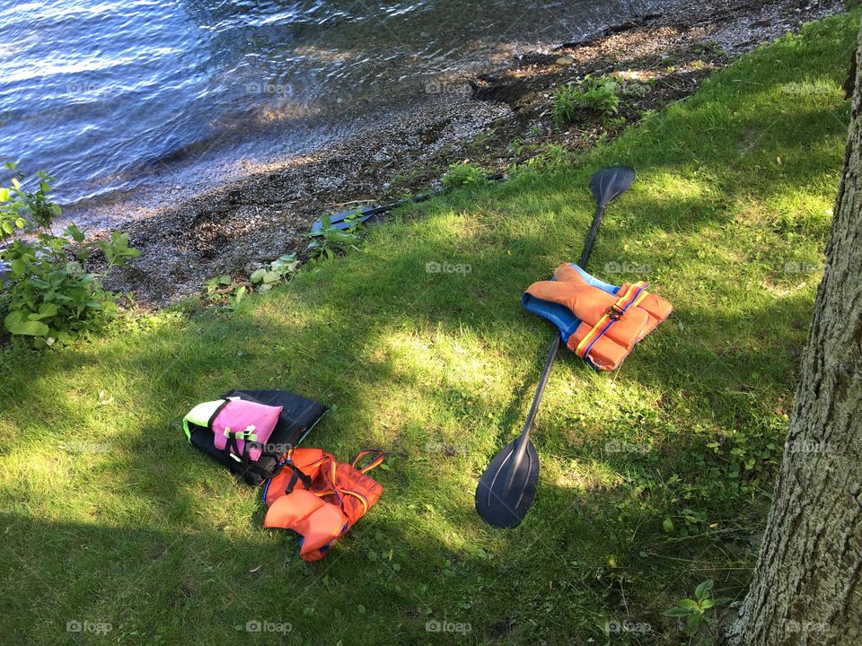 Orange retro life jackets on grass next to water front of lake on hill with paddle conceptual healthy lifestyle outdoor activity summer vacation background 