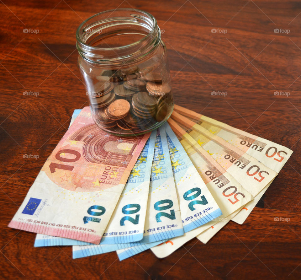 Euro cent coins in a glass jar and euro banknotes.
