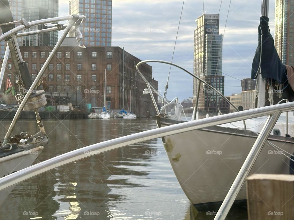 As the afternoon is approaching twilight time the setting sun illuminates the high rises with their glass facades causing them to gleam around the edges here at “Newtown Creek” by the “Pulaski Bridge” in LIC, Queens. 2023. Hypnotic Productions
