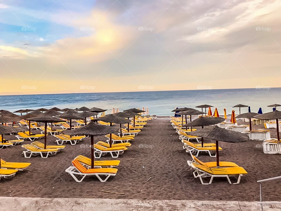 Chairs and umbrellas on a beach . chairs with orange mattresses . beach with black sand