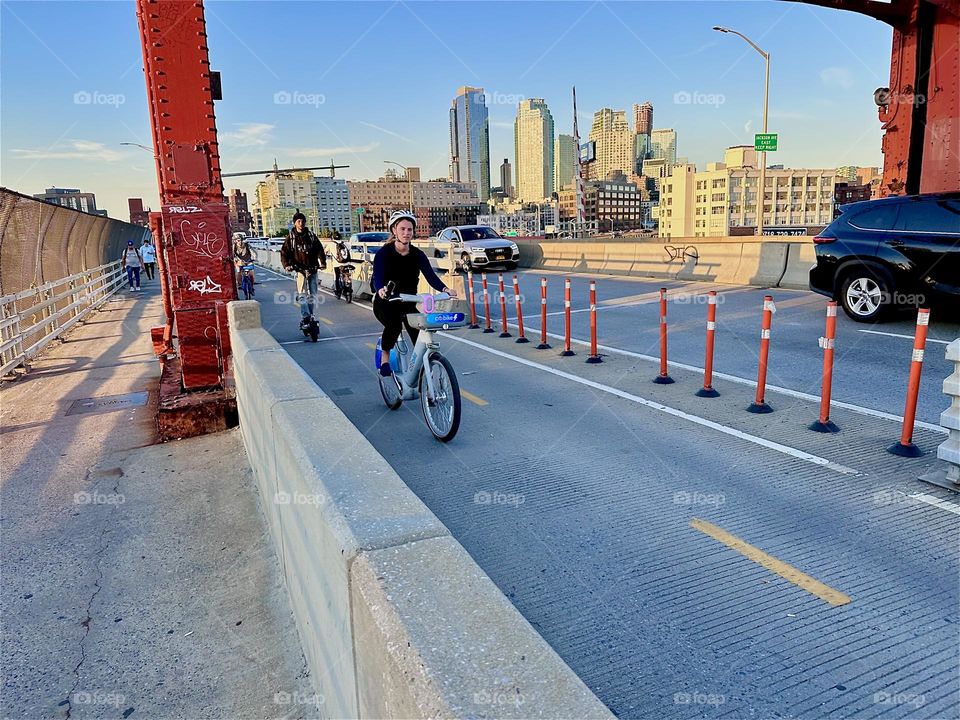 This is the “Pulaski Bridge” at “Newtown Creek” connecting “Greenpoint”, Bklyn to LIC in the direction we are currently heading. Upcoming bicyclists are cycling towards Brooklyn in the golden glow of the evening sun. 2024. Hypnotic Productions