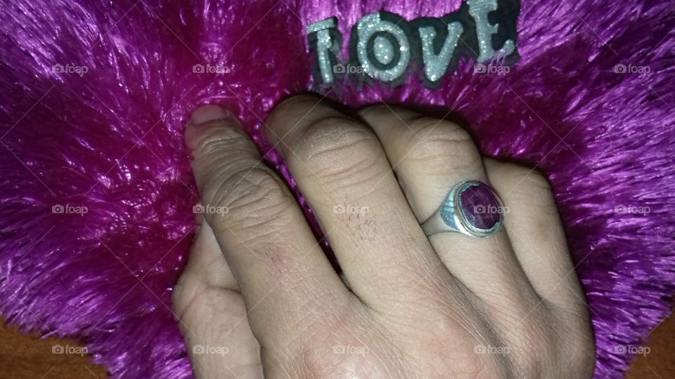 Close-up of man's hand wearing purple stone ring on pillow with love text