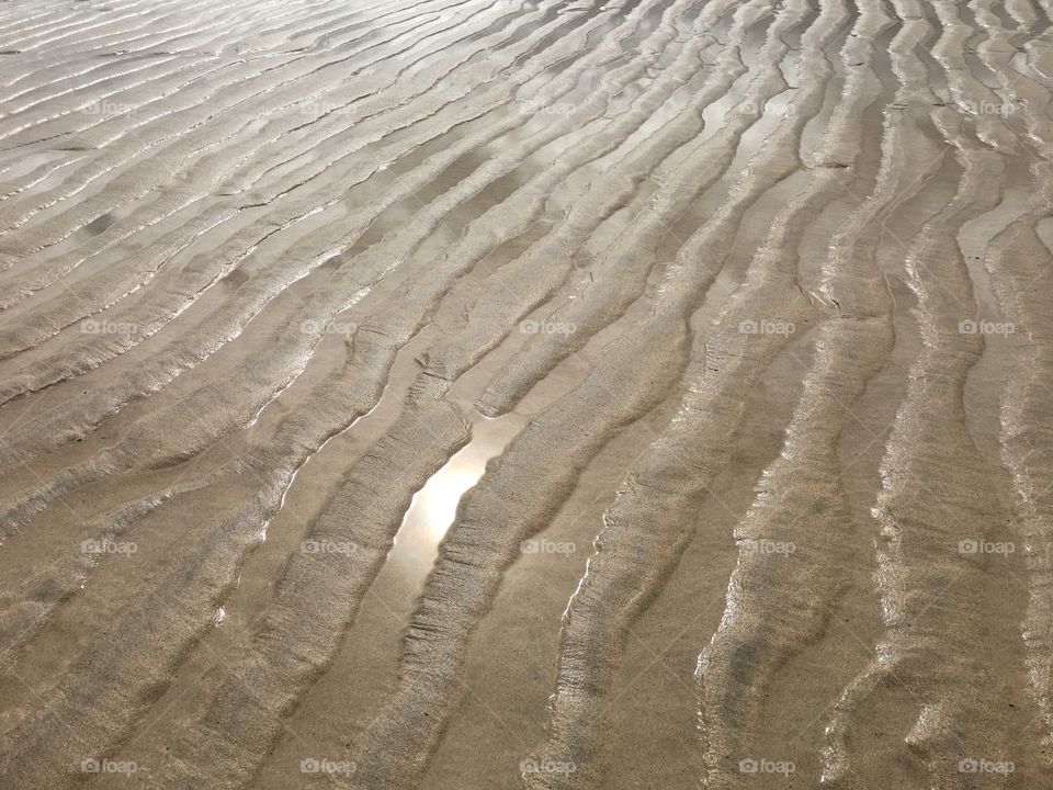 Sand textures with pools of water reflecting the sun. 