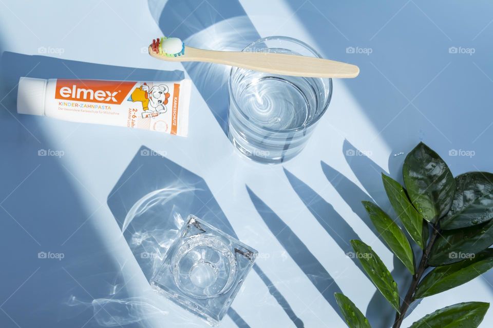 Elmex toothpaste for small children for oral and dental care, ecological toothbrush is on a blue background, with water, and a green flower.