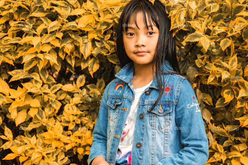 Portrait of a young little girl by the Autumn leaves.