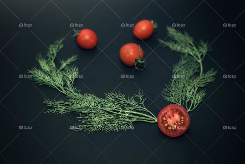 Ripe cherry tomatoes and a sprig of dill close-up. Vegetables isolated on a black background. Heart-shaped pattern from vegetables and greens
