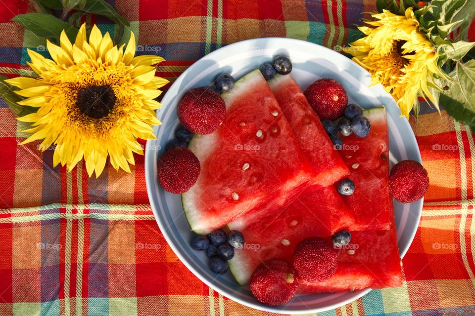 Fruity picknick on a colourful blanket with watermelon , blueberries and sunflowers.