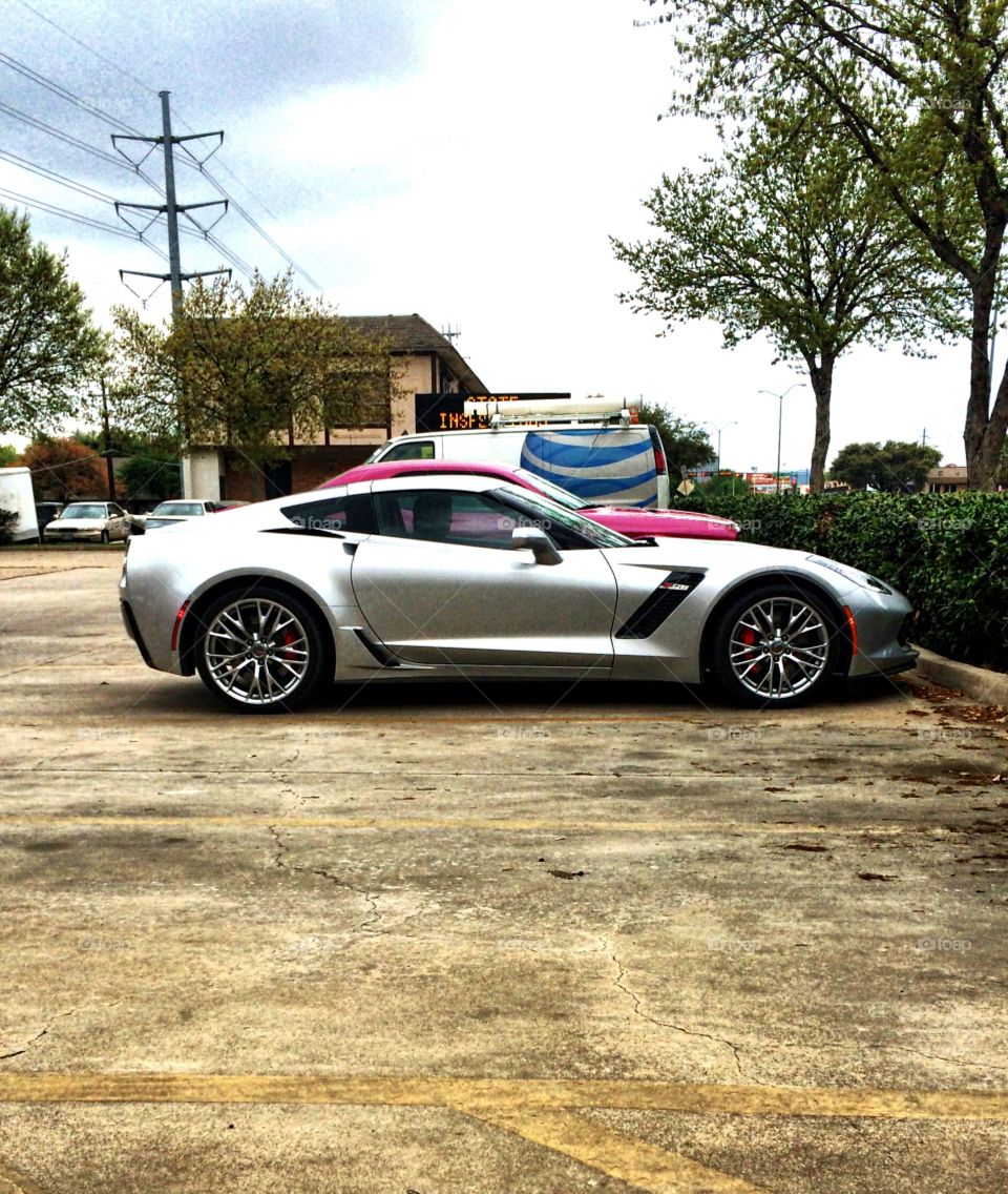 A silver Chevrolet Corvette with custom accenting in a city parking lot on a cloudy day.